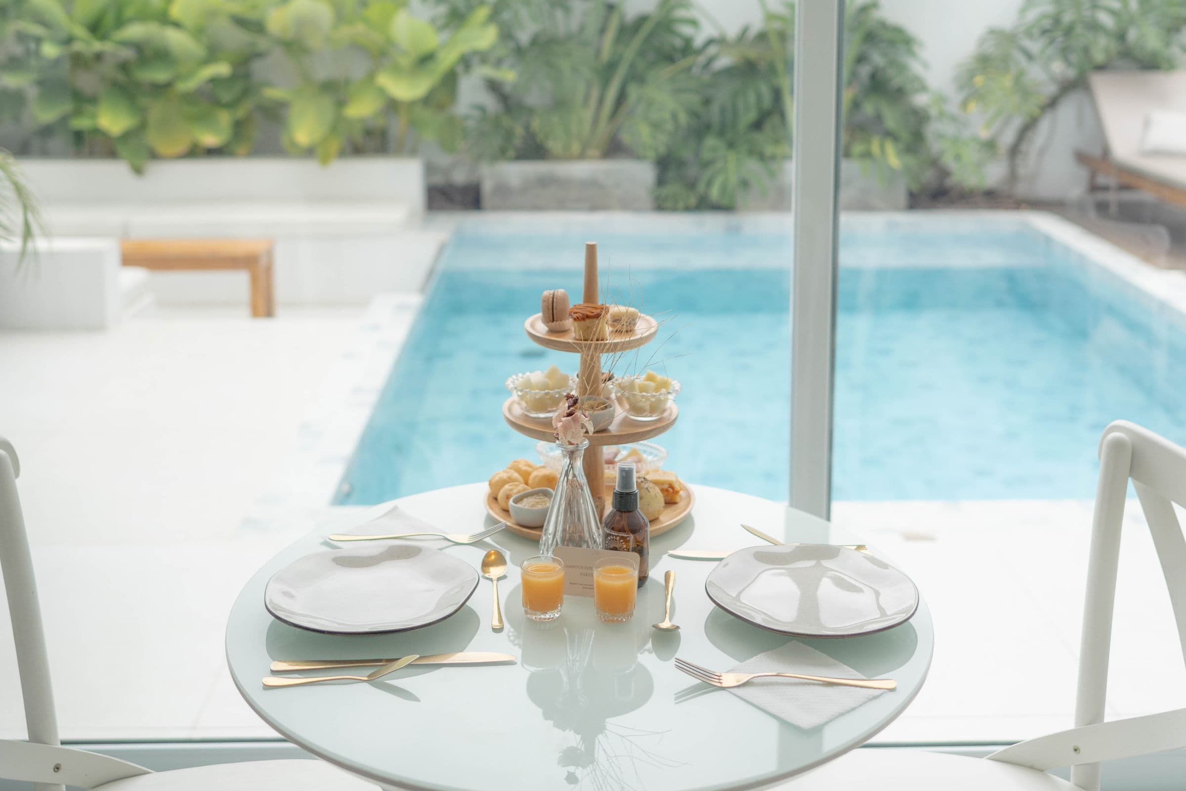 Mesa de café da manhã posta para dois diante do vidro, com a torre de doces e a piscina logo atrás
