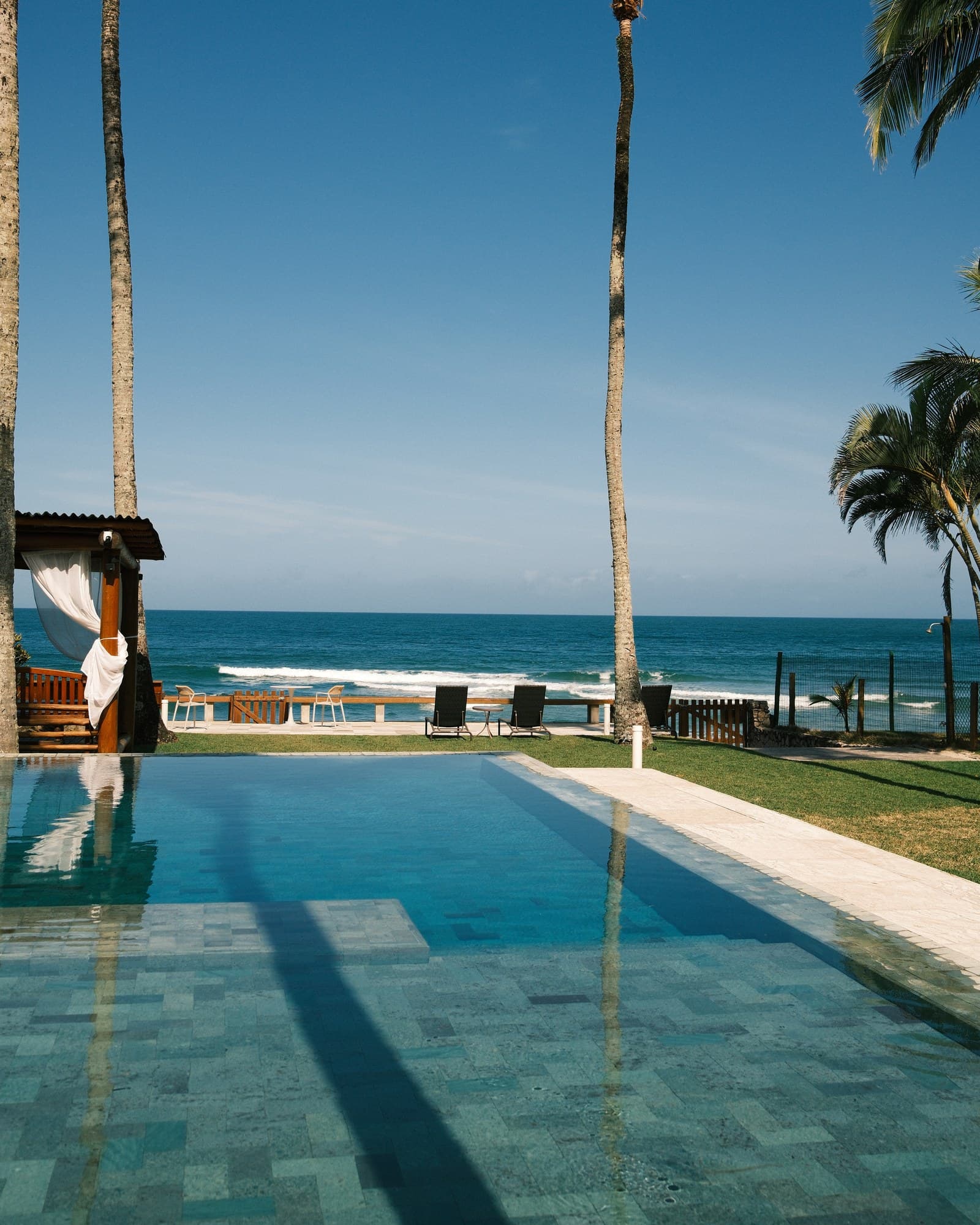 A piscina de beira-mar do OLISA Al Mar, entre coqueiros, com o mar aberto ao fundo