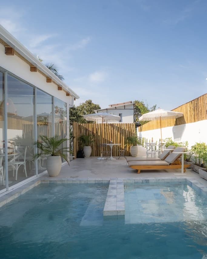 A piscina do OLISA Praia Hotel, com espreguiçadeiras de madeira junto ao prédio de vidro